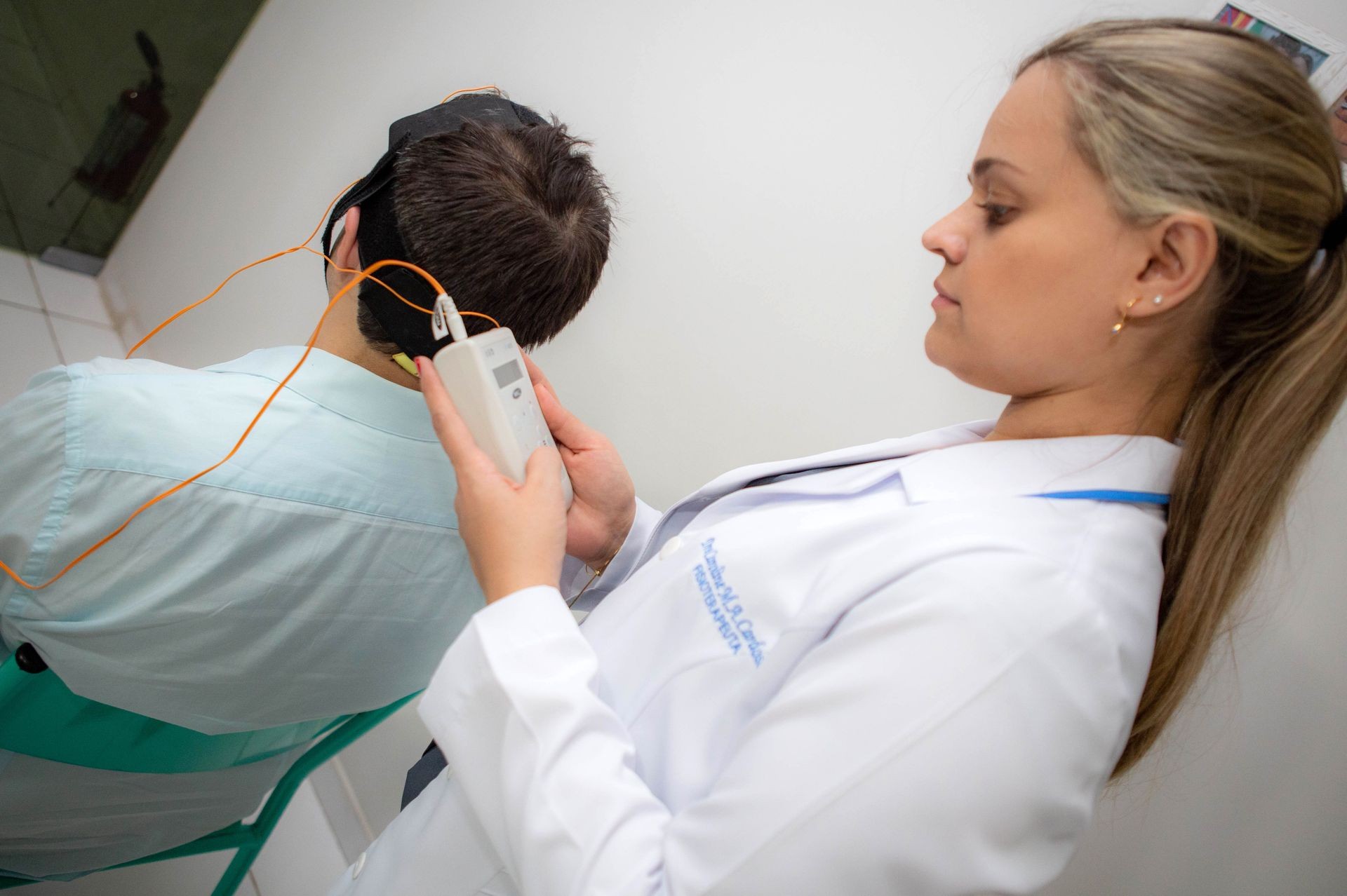 Healthcare professional using a diagnostic device on a patient with sensor cables attached to their head.