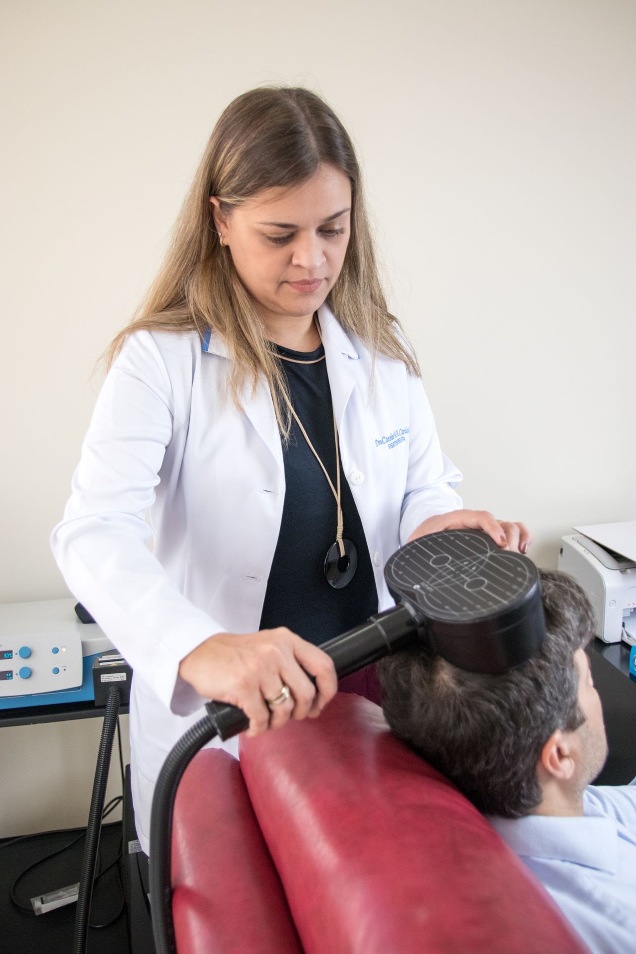 Medical professional using a large handheld device on the head of a seated patient in a clinical setting.