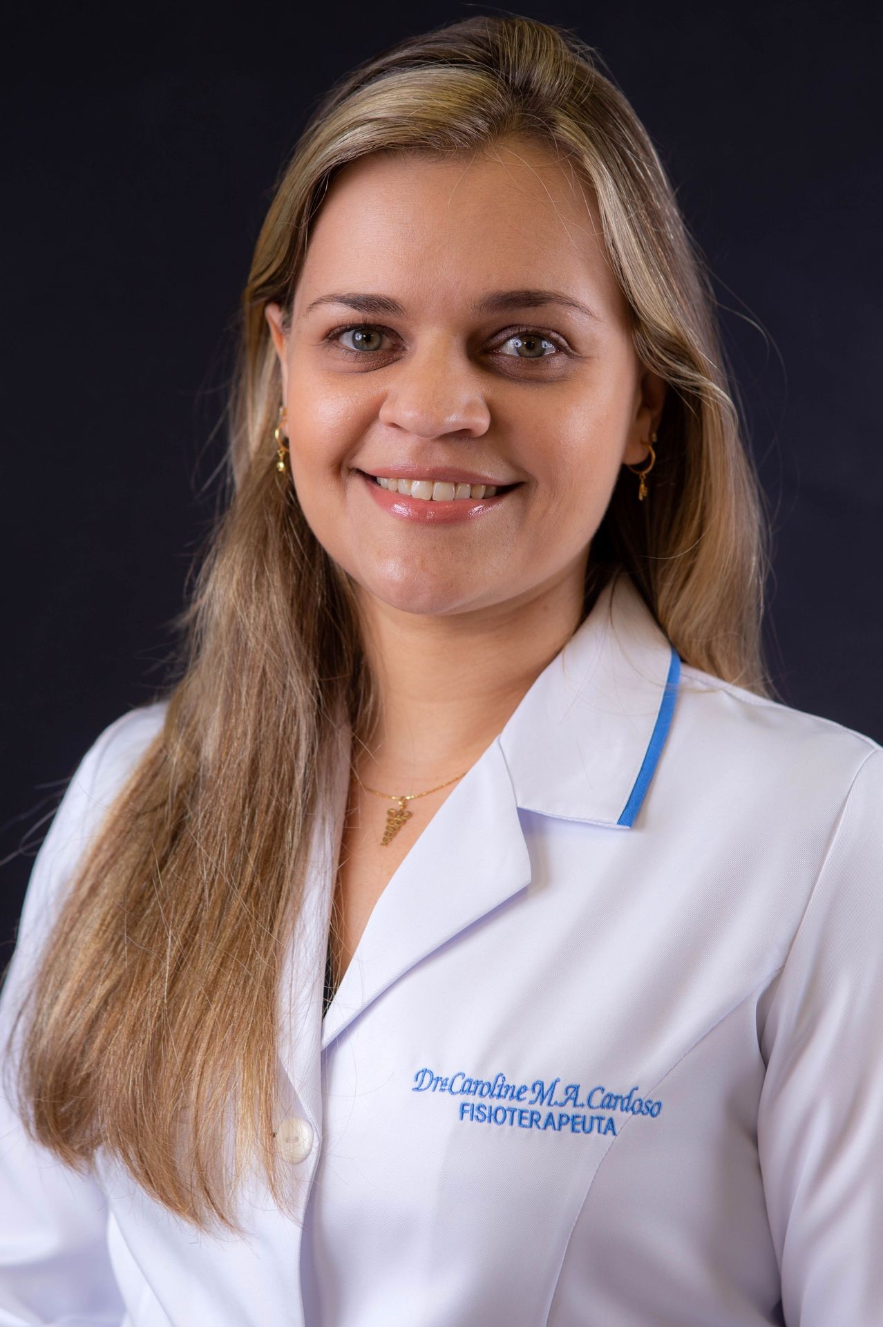 Smiling woman wearing a white lab coat with embroidered text, posing against a dark background.