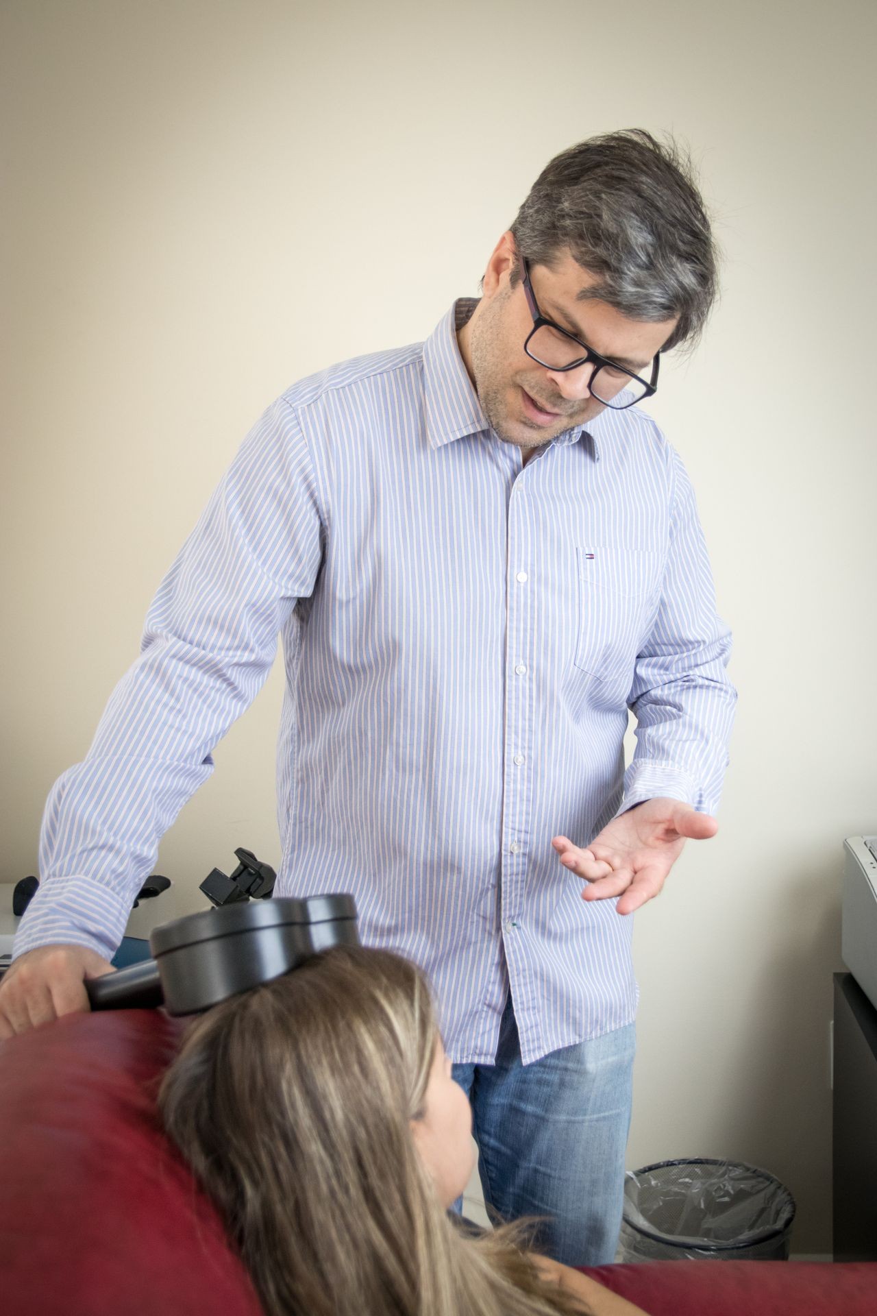 Person wearing a striped shirt holding a device near a woman's head in an indoor setting.